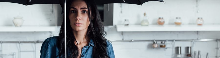 Amazed woman standing under umbrella during leak in kitchen