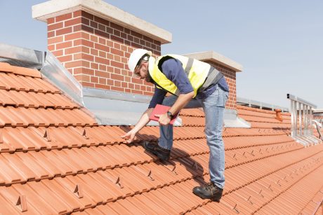 Product manager checking ventilation roof tiles in front of chimney standing on the roof wearing hard hat and safety jacket