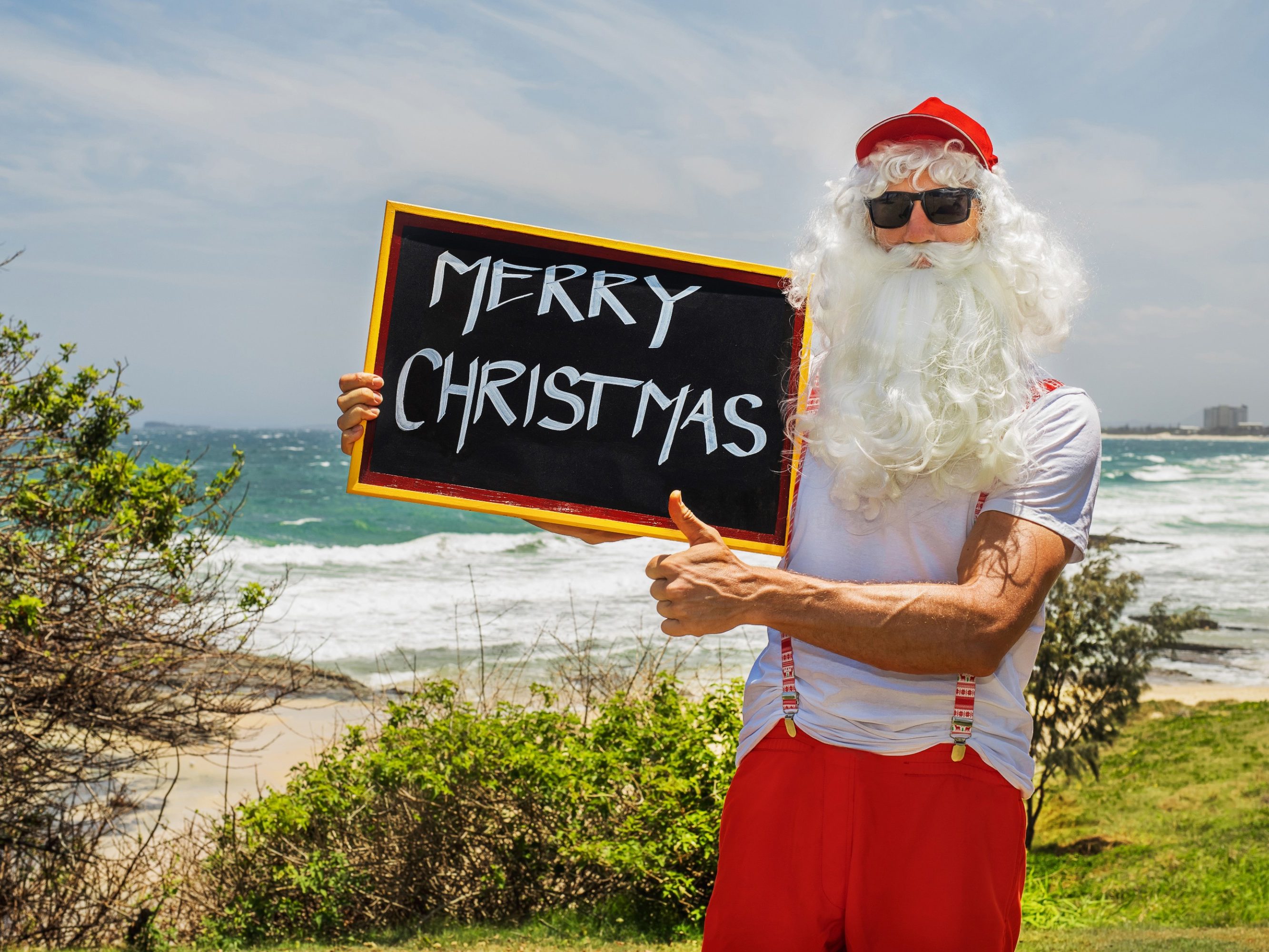 Santa Claus holds gift boxes with the ocean on backgraund. Australia, Christmas in summer time.