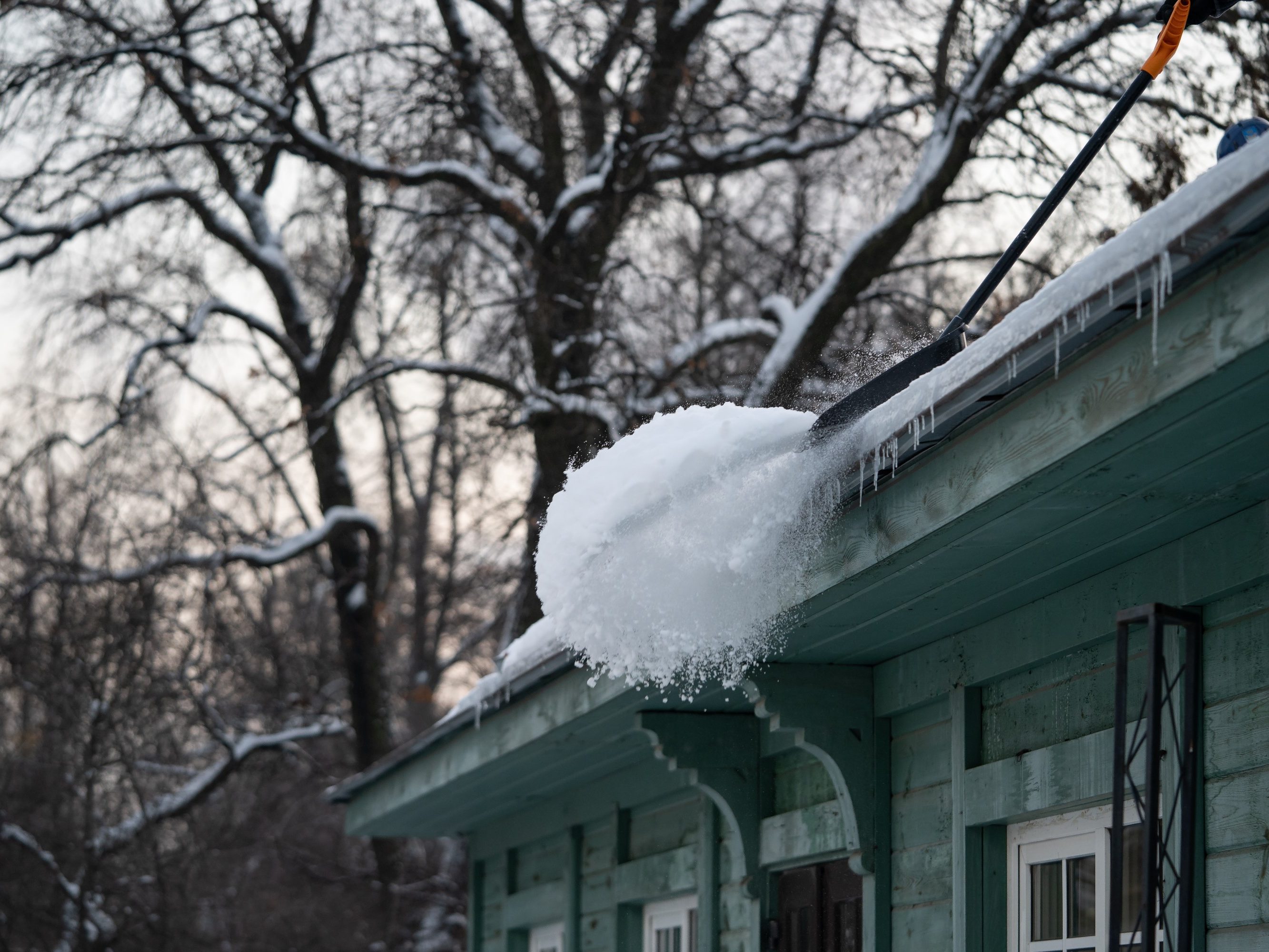 Cleaning roof from snow with shovel. Danger of getting injured from snow or icicles falling from rooftop. Workers removing snow from old wooden building. Wintertime maintenance and activity concept