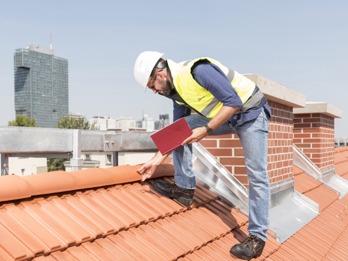 Urban roofers builder standing on roof checking toof tiles wearing hard hat and safety jacket