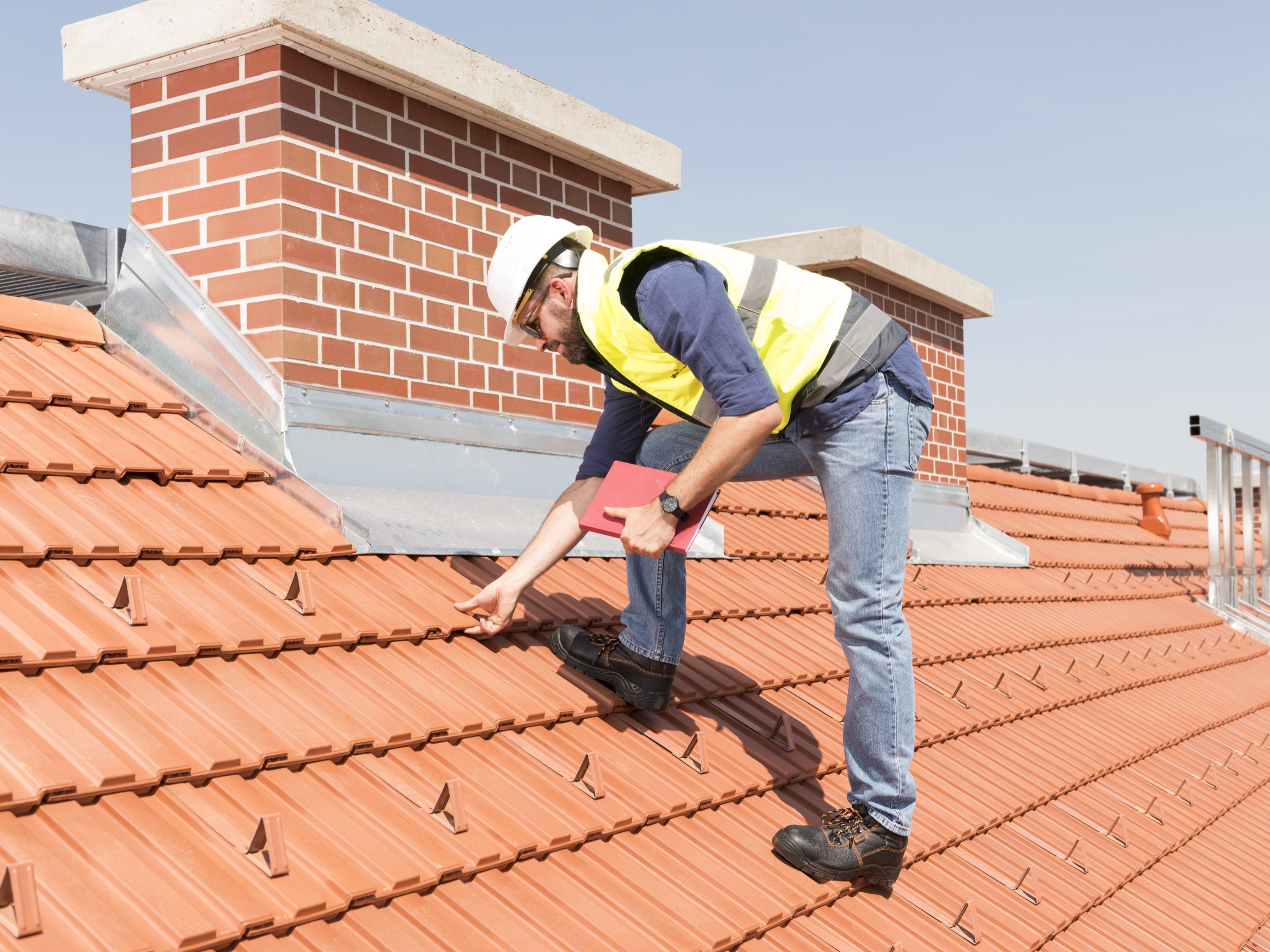 Product manager checking ventilation roof tiles in front of chimney standing on the roof wearing hard hat and safety jacket