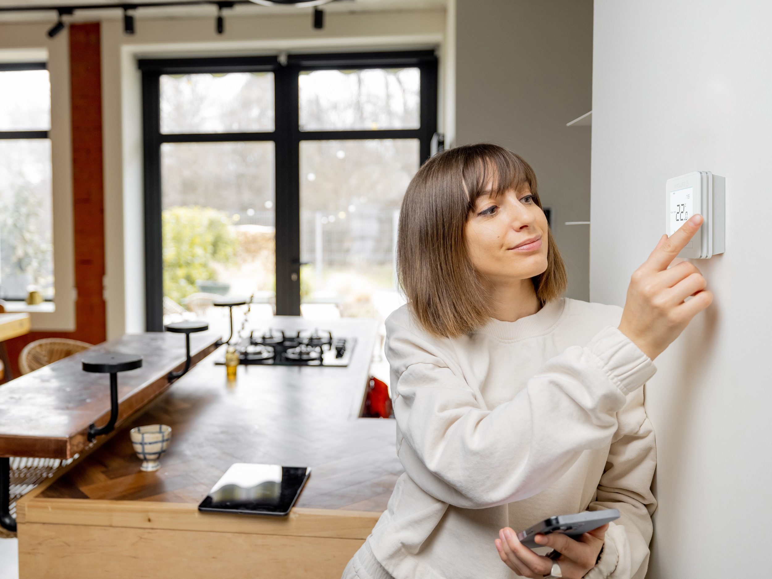 Woman controlling home temperature with electronic thermostat mounted on the wall in living room at home. Concept of modern technologies and smart home | Pipelife