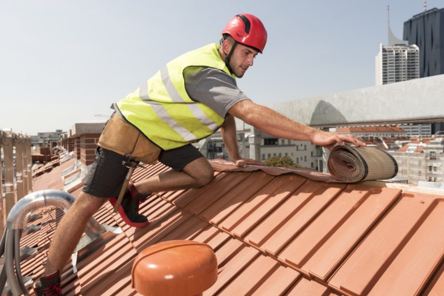 Roofer applying Alu-Grip Rol ridge and hip roll on ridge wearing safety jacket and hard hat