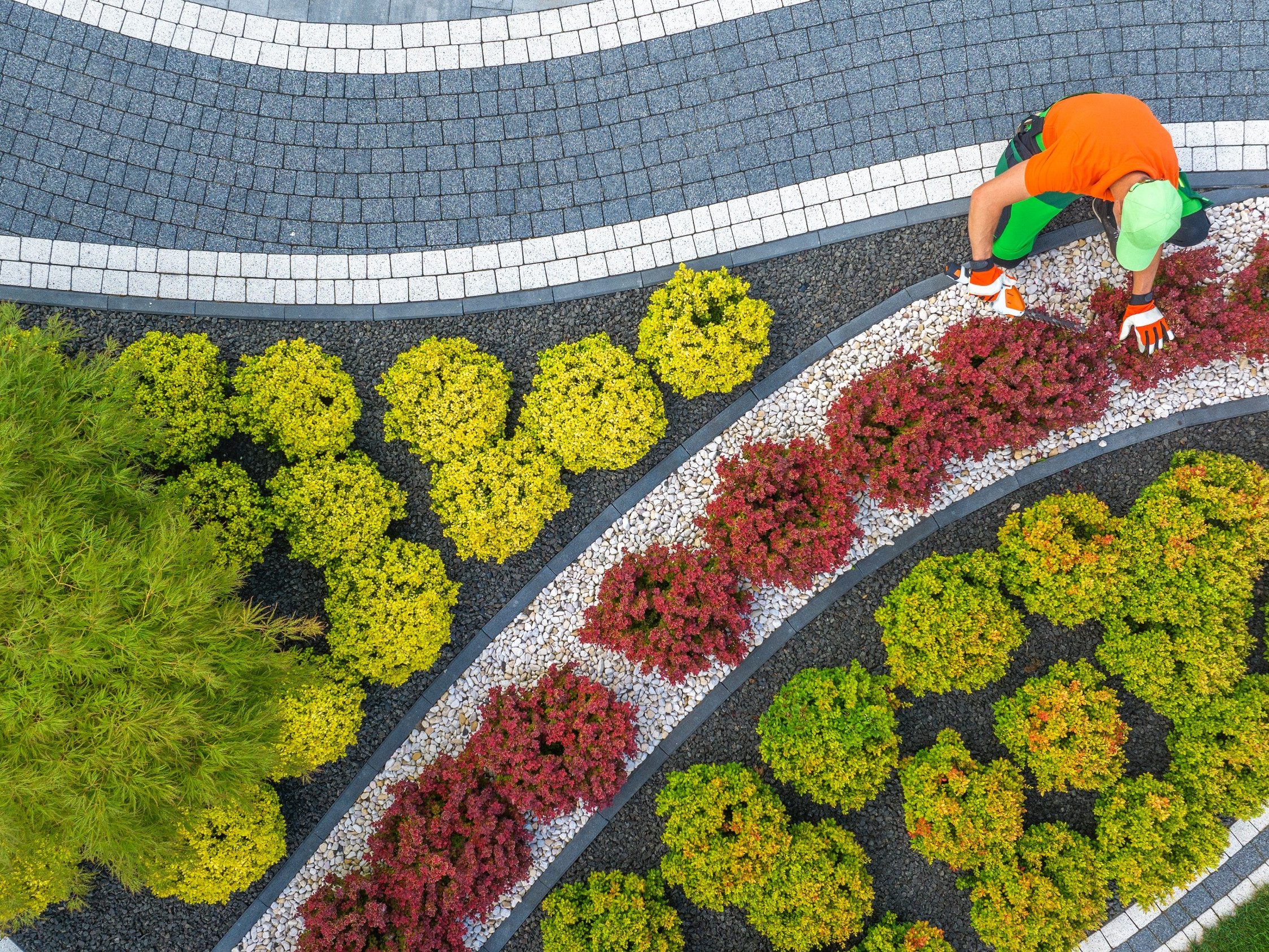 Aerial View of Caucasian Gardener in His 40 Shaping Back Yard Garden Plants Using Cordless Trimmer