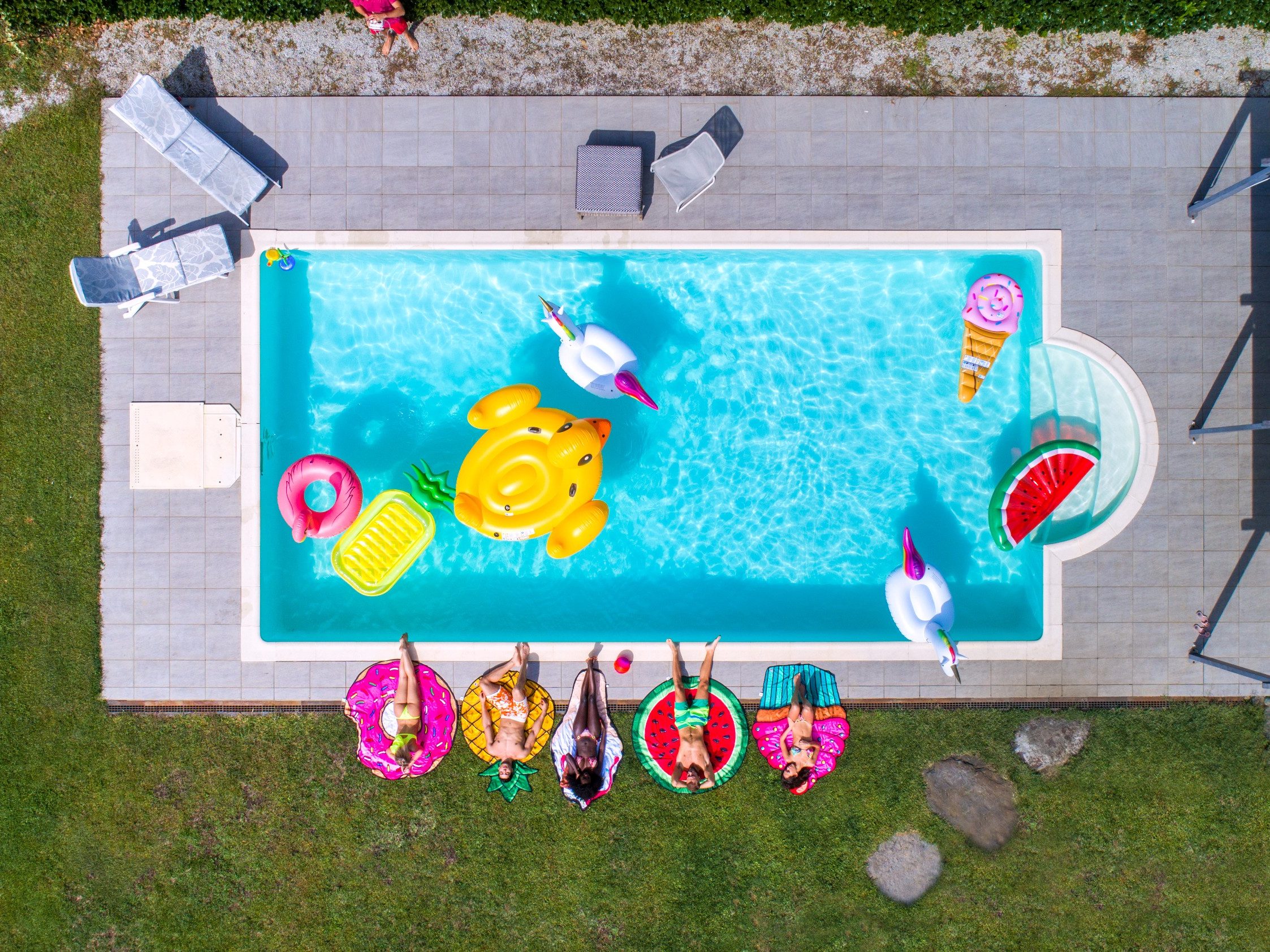 Happy people partying in an exclusive swimming pool with animal and fruit shapes mats, view from above