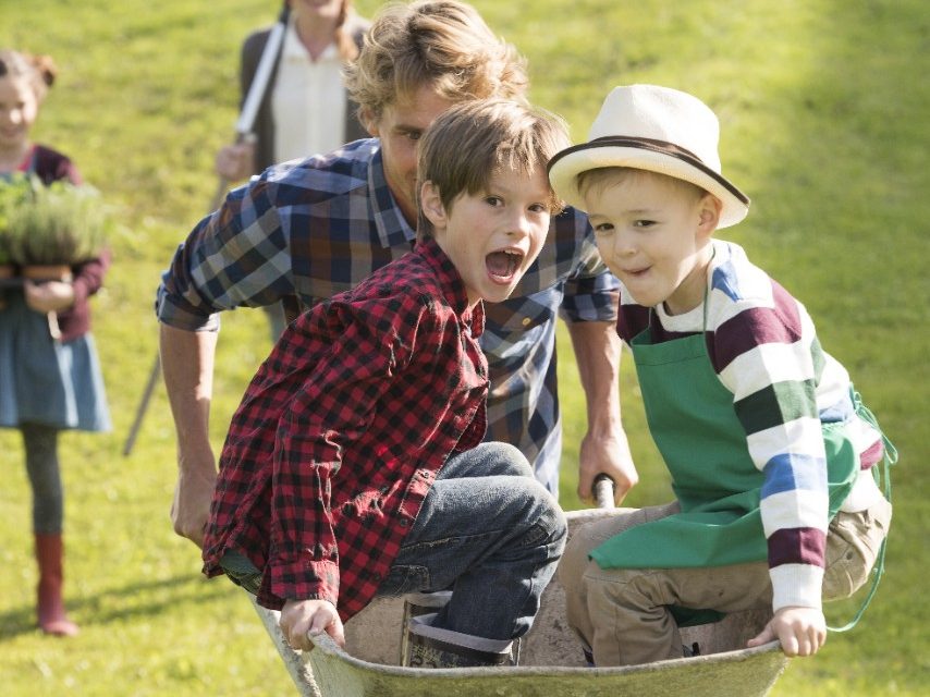 Wheelbarrow fun with adult man and two boys, girl and adult woman in background