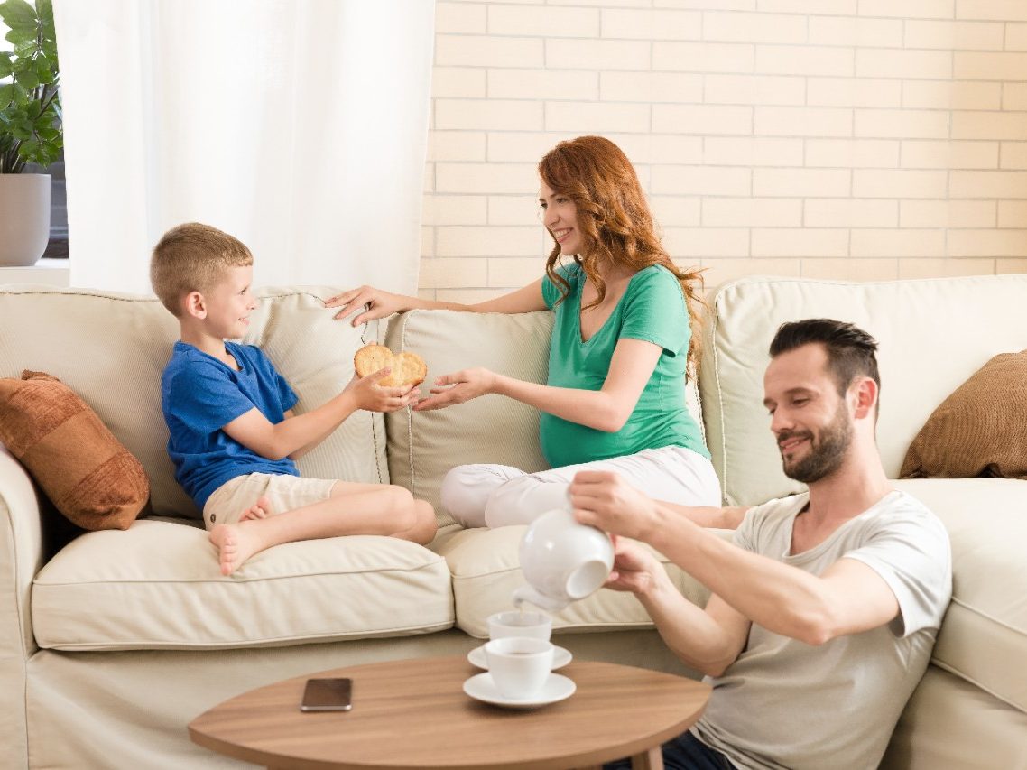 Boy handing over a cookie heart to his mother while father is pouring tea into cups