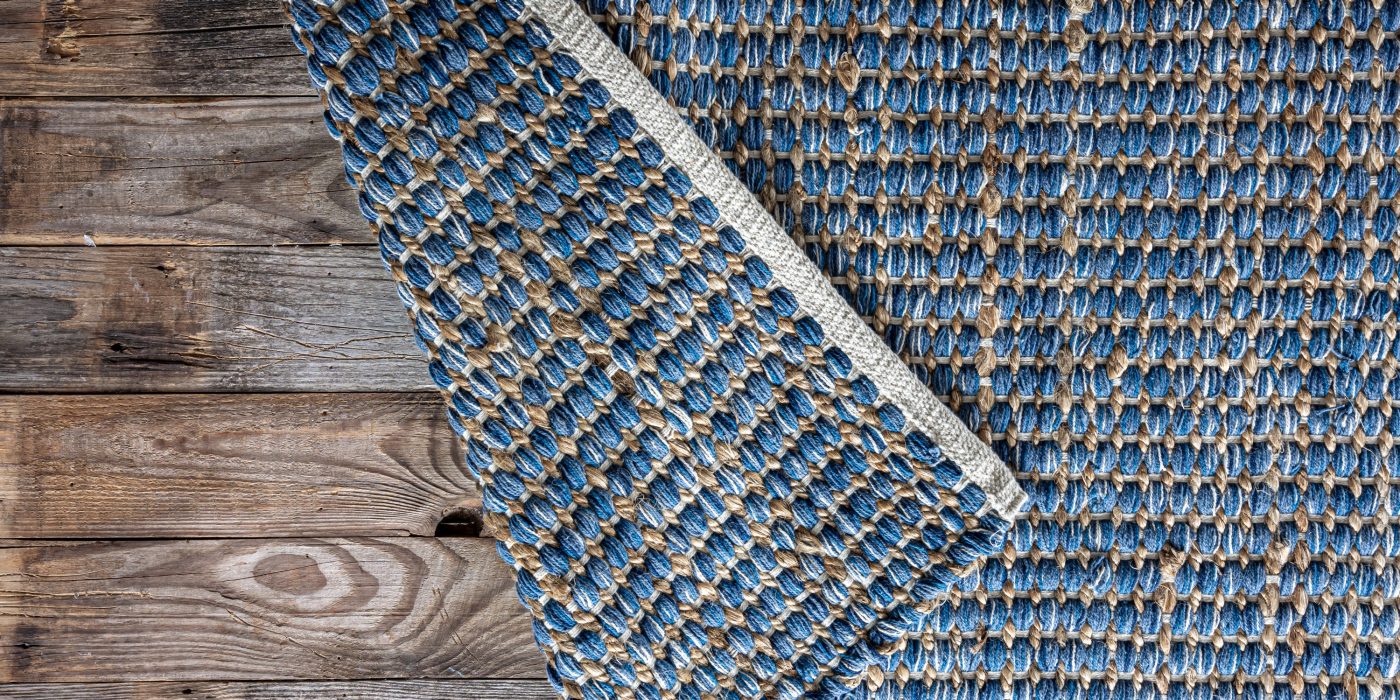 Hand woven geometric denim area rug on a wooden floor, jute braided home background texture, top view, copy space.