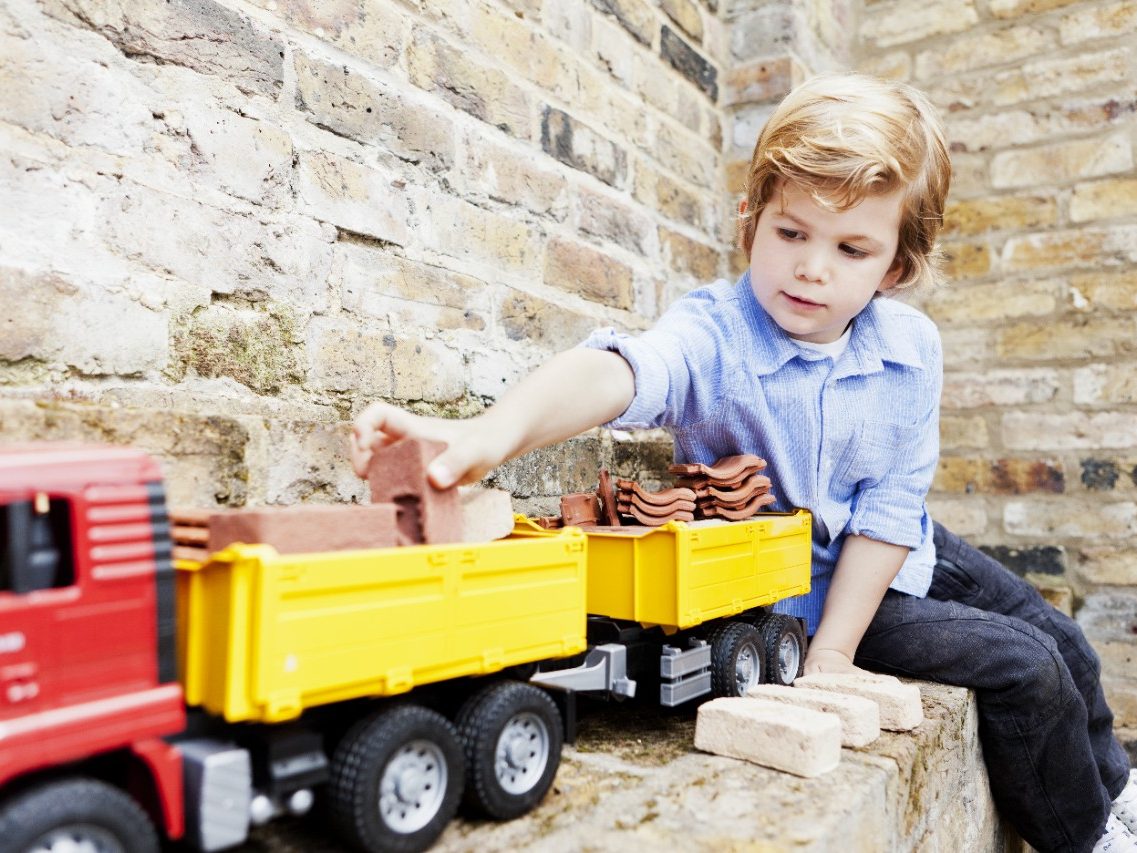 Boy loading miniature bricks and clay roof tiles on toy truck