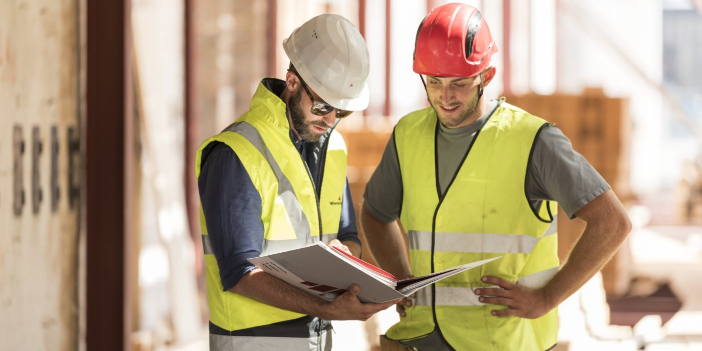 Product manager and roofer talking checking product information in attic under renovation