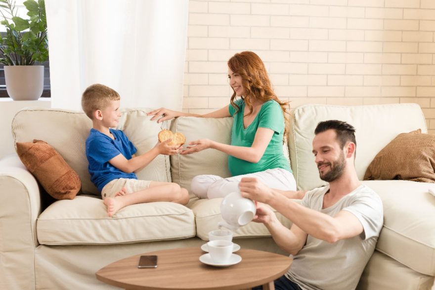 Boy handing over a cookie heart to his mother while father is pouring tea into cups