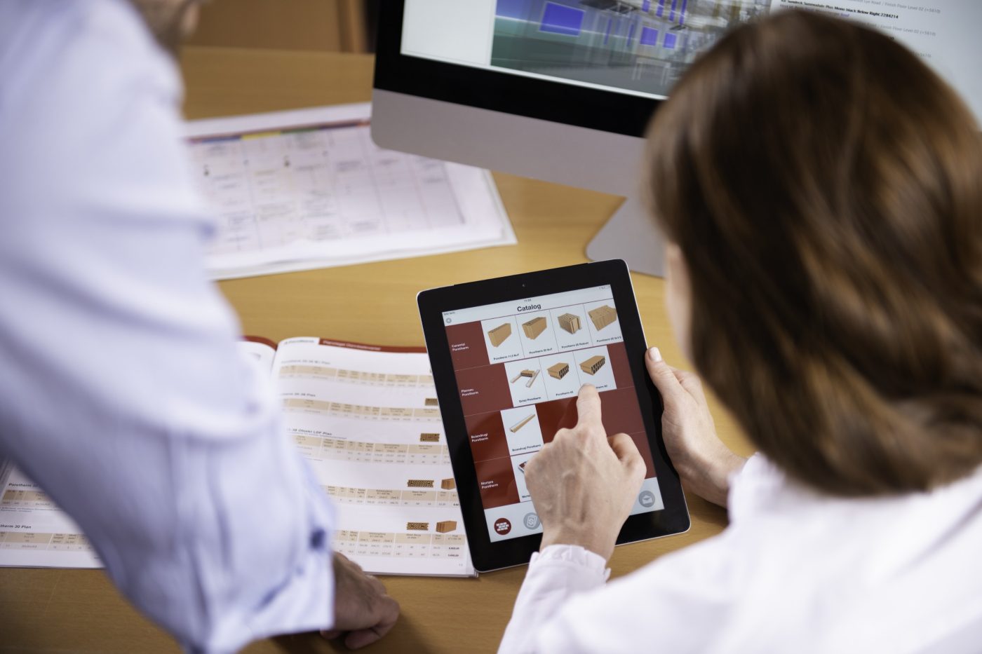 Woman at workplace holding tablet computer sitting next to standing man