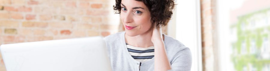 Woman looking at computer screen in front of brick-lined wall