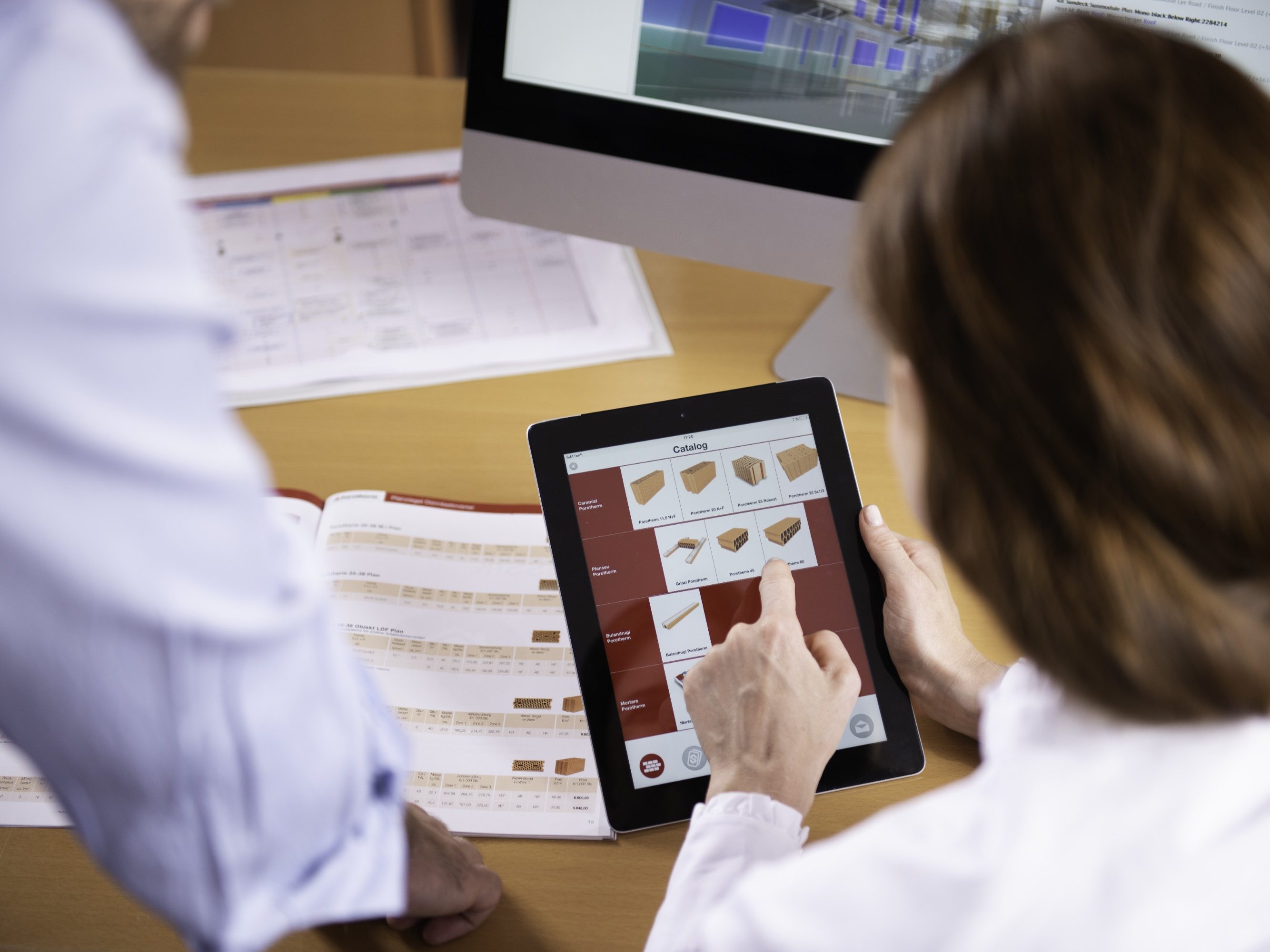 Woman at workplace holding tablet computer sitting next to standing man